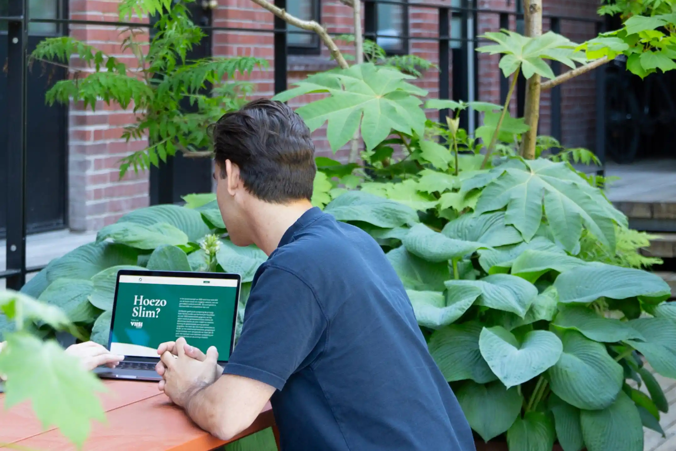 Woningzoeker bekijkt het SlimBieden woningrapport op een laptop in de tuin